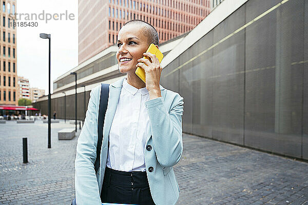Lächelnde Geschäftsfrau  die vor dem Gebäude mit dem Smartphone spricht