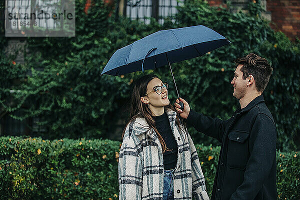 Junger Mann gibt seiner Freundin vor Pflanzen einen Regenschirm