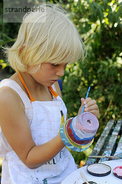 Little girl painting flower pots in garden