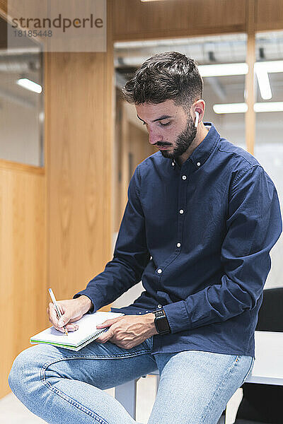Junger Geschäftsmann schreibt Tagebuch und sitzt am Schreibtisch im Büro