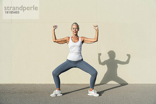 Frau macht an einem sonnigen Tag Sport vor einer cremefarbenen Wand