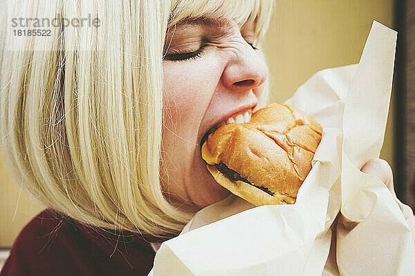 Frau mit blonden Haaren isst Hamburger