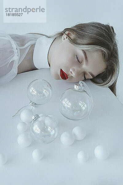 Beautiful girl with eyes closed sleeping by Christmas balls on table