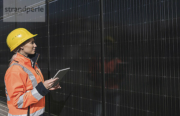 Junge Ingenieurin mit Tablet-PC untersucht Sonnenkollektoren an einem sonnigen Tag