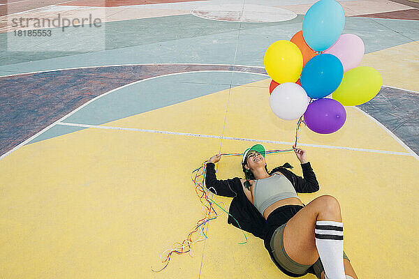 Glückliche Frau mit bunten Luftballons auf dem Sportplatz liegend
