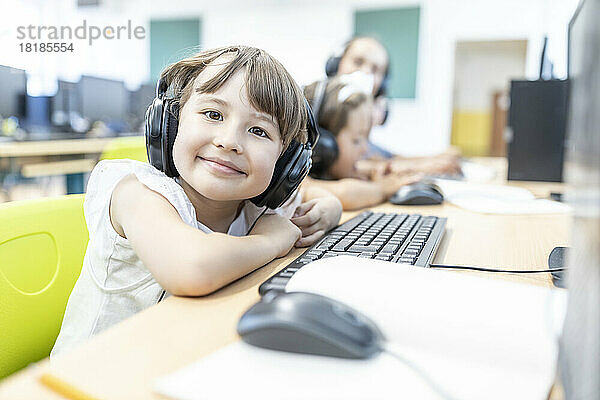 Smiling schoolgirl wearing headphones in computer class at school