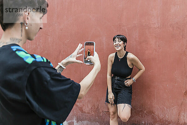 Junger Mann fotografiert Freundin mit Smartphone vor roter Wand