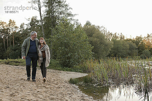 Mann und Frau gehen gemeinsam im Sand am See spazieren