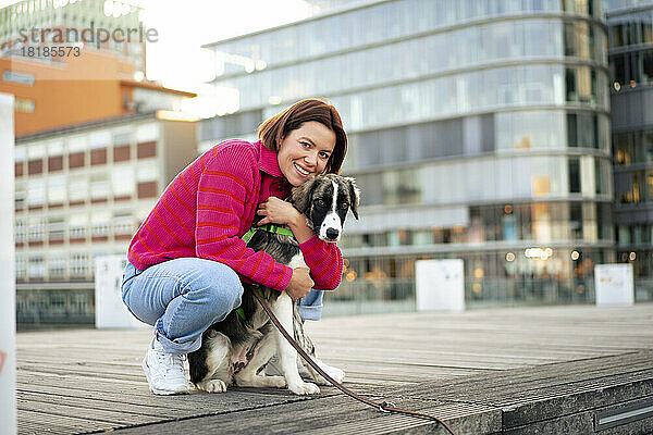 Lächelnde Frau umarmt Hund  der am Pier kauert