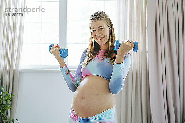 Lächelnde schwangere Frau  die zu Hause mit Hanteln trainiert
