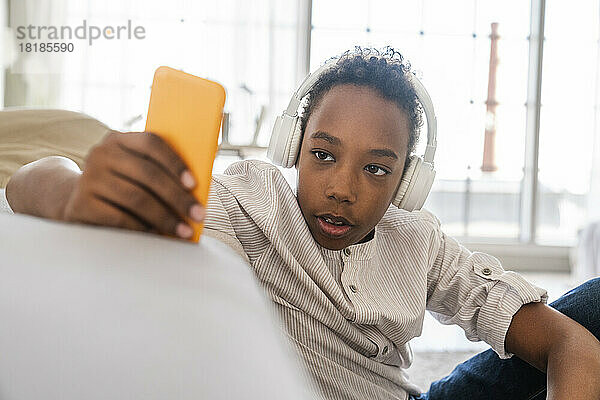 Junge benutzt Mobiltelefon  trägt Kopfhörer und hört zu Hause Musik