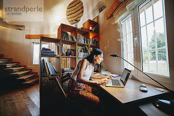 Reife Frau sitzt mit Laptop am Tisch zu Hause