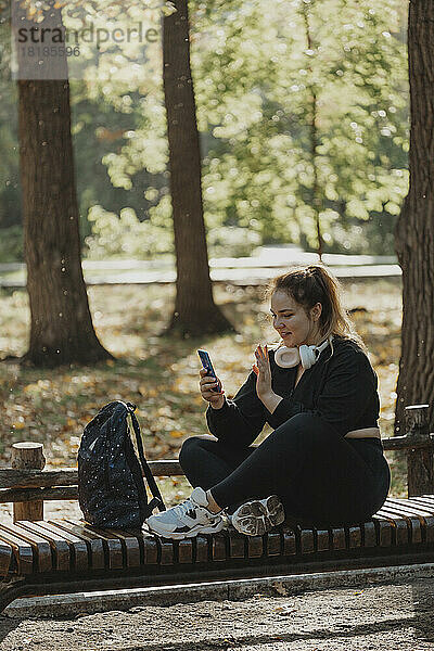 Lächelnde Frau  die auf einer Bank im Park einen Videoanruf über ihr Smartphone führt