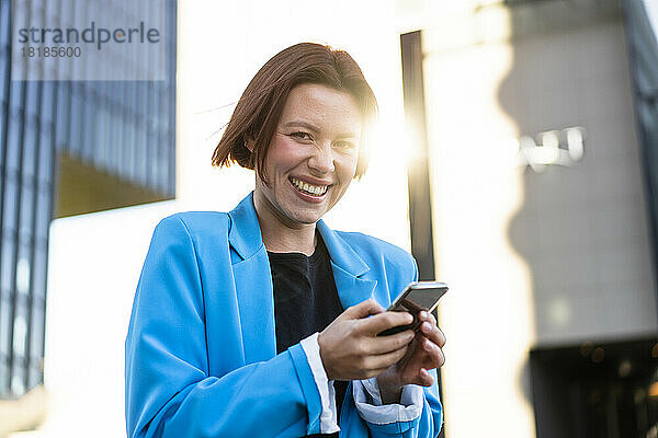 Junge Geschäftsfrau mit Smartphone lacht an sonnigem Tag