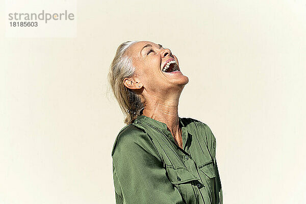 Mature woman laughing in front of cream colored wall