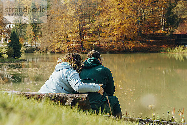 Frau umarmt Mann  der auf Bank am See sitzt
