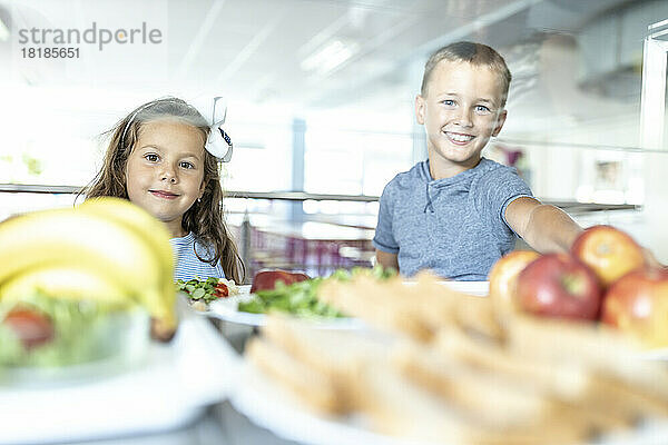 Lächelnde Grundschüler essen in der Mittagspause Obst in der Schulkantine