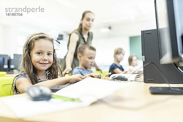Lächelnder Grundschüler  der in der Computerklasse in der Schule sitzt