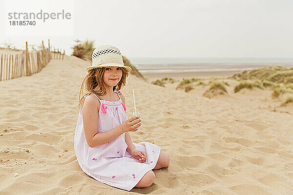 Porträt eines Mädchens  das am Strand sitzt und etwas trinkt