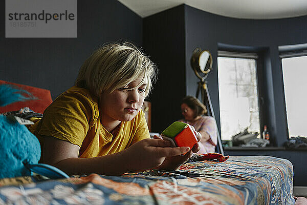 Junge spielt mit Puzzle-Würfel und liegt zu Hause im Bett