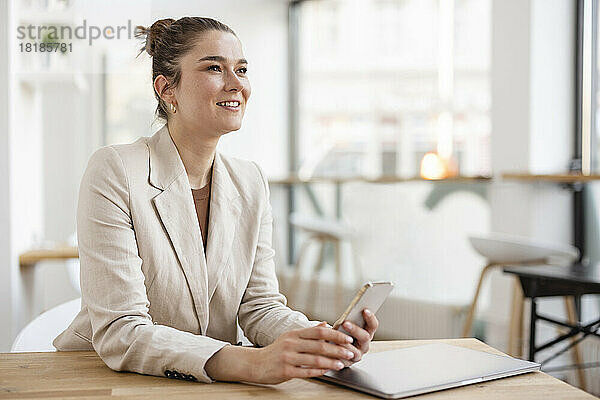 Lächelnde Geschäftsfrau mit Mobiltelefon und Laptop am Schreibtisch