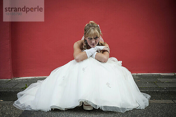 Germany  Rhineland-Palatinate  portrait of bride sitting on curb in front of red facade