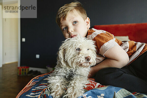 Cute boy embracing dog on bed in bedroom