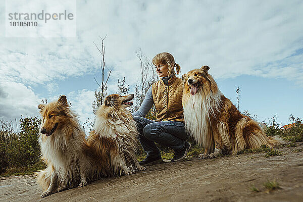 Woman with collie dogs crouching under cloudy sky