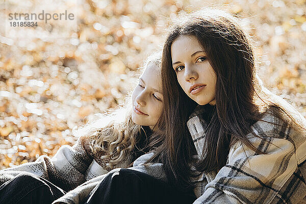 Mädchen mit Schwester sitzt an sonnigem Tag im Wald
