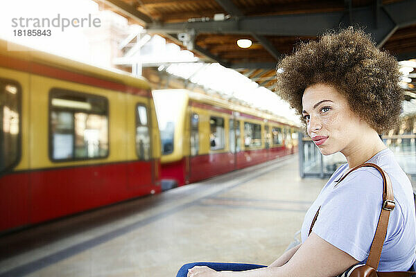 Junge Frau sitzt auf einer Bank am Bahnhof