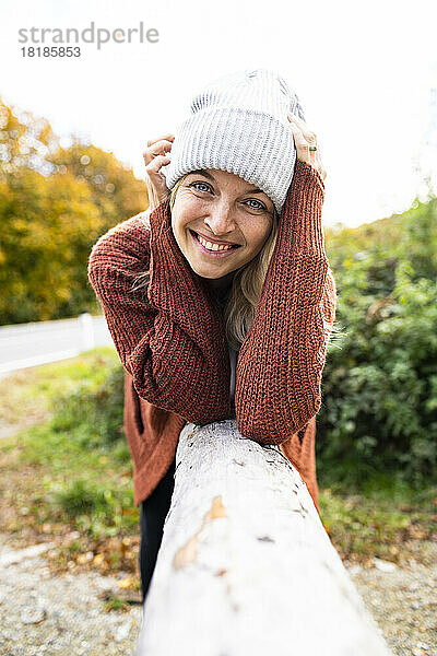 Lächelnde reife Frau  die sich im Herbst an Holz lehnt