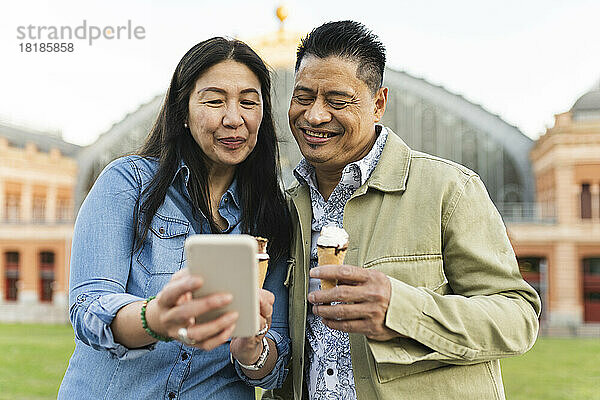 Lächelnde Frau  die Eis isst und dem Mann ihr Mobiltelefon zeigt