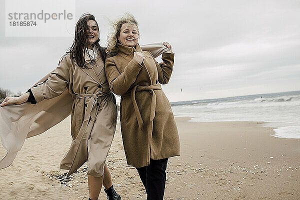 Mutter und Tochter tragen Mäntel und amüsieren sich am Strand