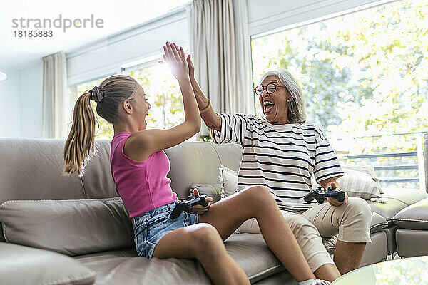 Fröhliche ältere Frau gibt ihrer Enkelin  die zu Hause ein Videospiel spielt  ein High-Five