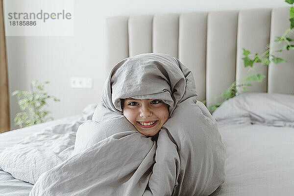 Happy girl wrapped in blanket on bed at home