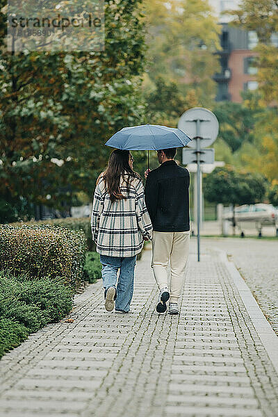 Junges Paar geht gemeinsam unter Sonnenschirm auf Fußweg spazieren