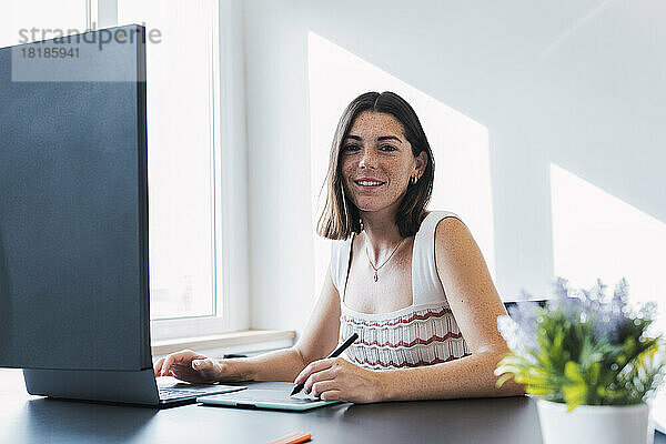 Junge Geschäftsfrau mit Sommersprossen sitzt vor dem Desktop-PC