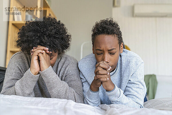 Mutter und Sohn beten mit geschlossenen Augen zu Hause am Bett