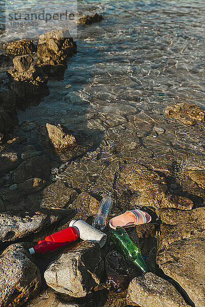 Leere Plastikflaschen und Hausschuhe schwimmen am Strand auf dem Wasser