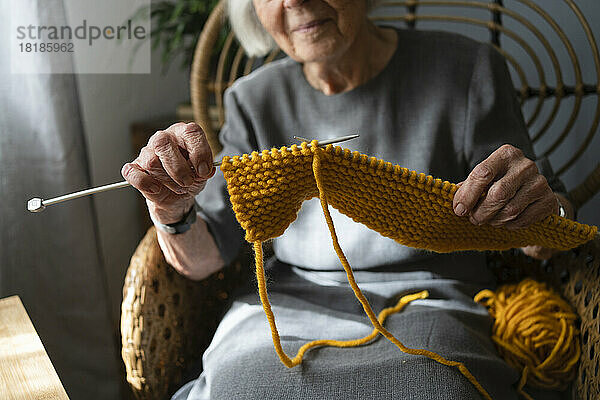 Hände einer älteren Frau  die zu Hause einen Schal strickt