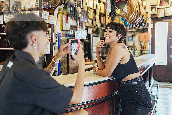 Mann fotografiert Freundin mit Handy in Feinkostladen