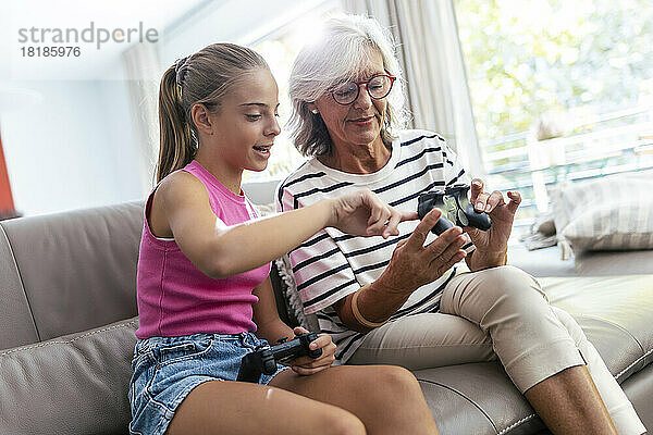 Enkelin spricht mit Großmutter und hält Joystick zu Hause auf dem Sofa