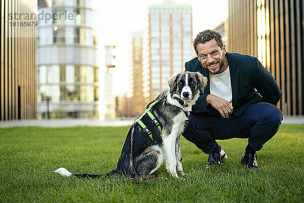 Lächelnder Geschäftsmann mit Hund  der auf Gras kauert