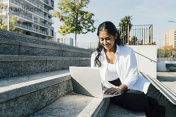 Lächelnde junge Frau benutzt Laptop auf Stufen