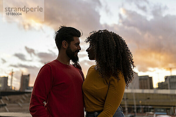 Happy young couple standing under sky at sunset