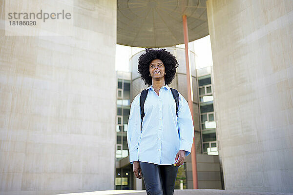 Glückliche junge Geschäftsfrau mit Afro-Frisur  die vor dem Bürogebäude läuft