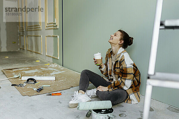 Junge Frau mit Einwegkaffeetasse lacht in der Wohnung