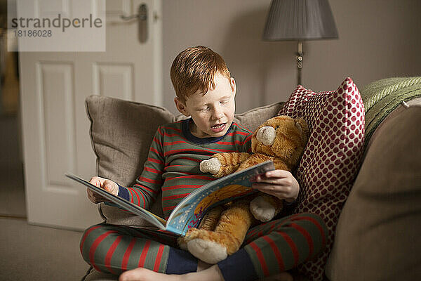 Boy reading a book on couch at home