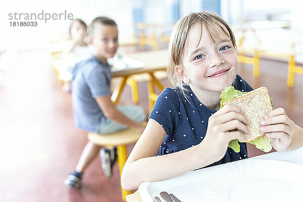 Smiling student holding sandwich at lunch break in cafeteria