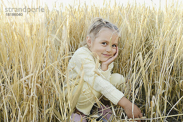 Smiling girl crouching amidst plants in field